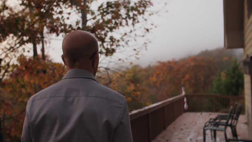 A man walks along a balcony looking out at the fall colors