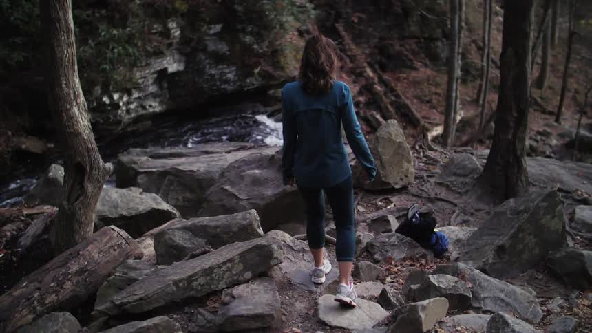 A woman walks down a rocky slope in the forest