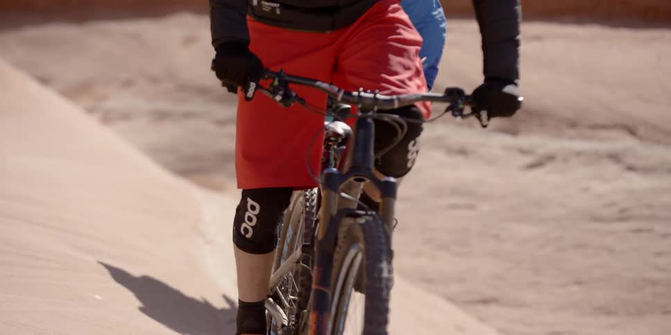 Two people bike up a sand dune