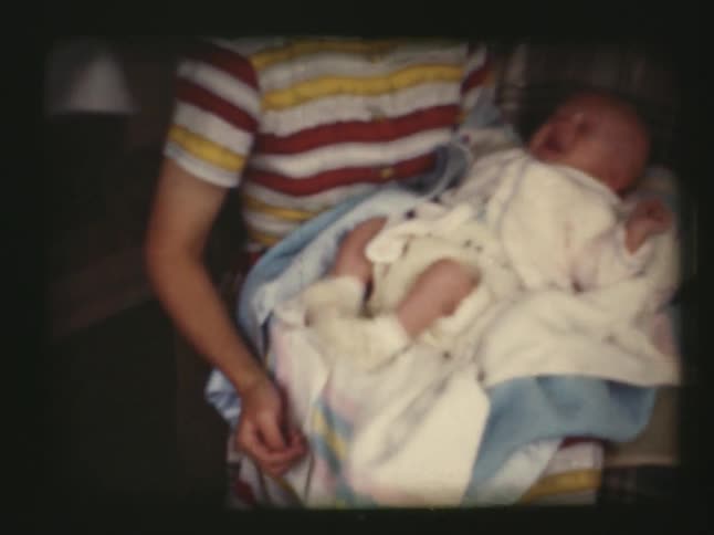 A person holds a crying newborn on a couch