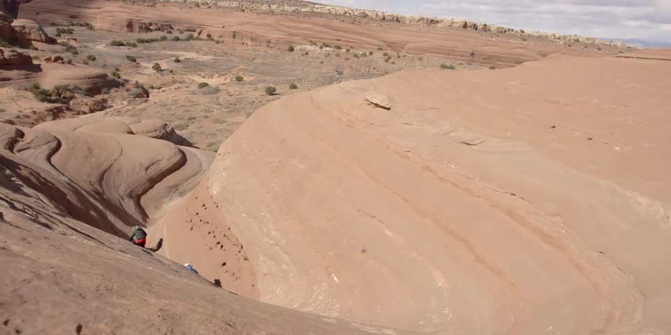 Two people ride bicycles down a cliff towards a canyon