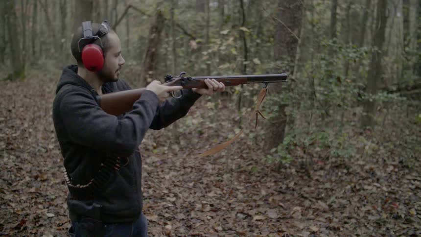 Man wearing ear muffs aiming gun in forest