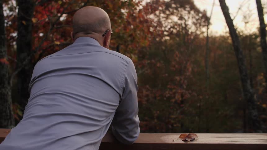 A man looks at fall trees from a deck at sunset