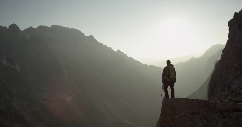 A man stands on a cliff while hiking in the mountains