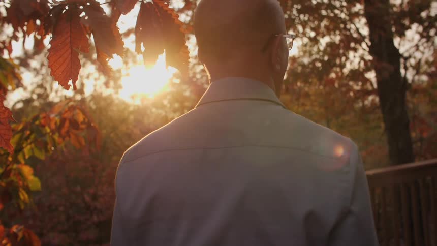 A man stands on a balcony looking towards the sun setting