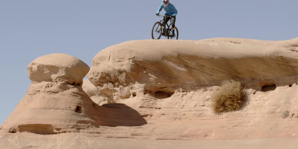 A man on a bike jumps from a tall rock