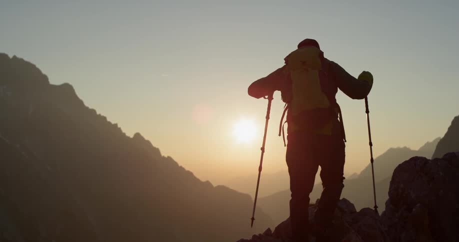 A man hikes on a mountain as the sun shines brightly