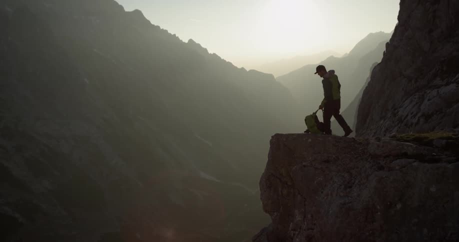 A hiker stops to sit on a cliff in the mountains