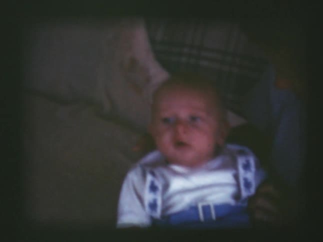 A woman holds an infant boy while sitting on a couch