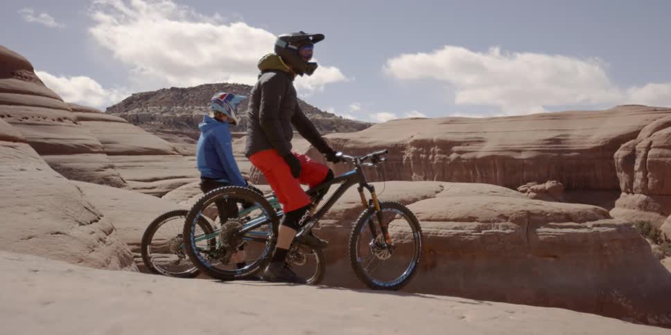 Two people on bikes overlooking cliffs on a sunny day