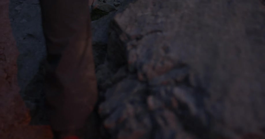 A man is using hiking poles as he hikes up a boulder strewn hillside