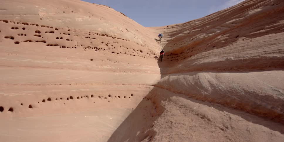 Bicyclists ride down a dune towards a canyon