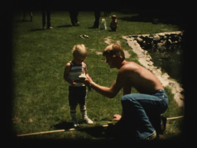 A man tries to hand a wiggling fish to a child