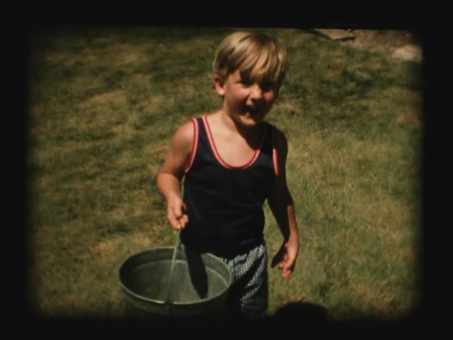 A young boy holds a metal pail on a lawn
