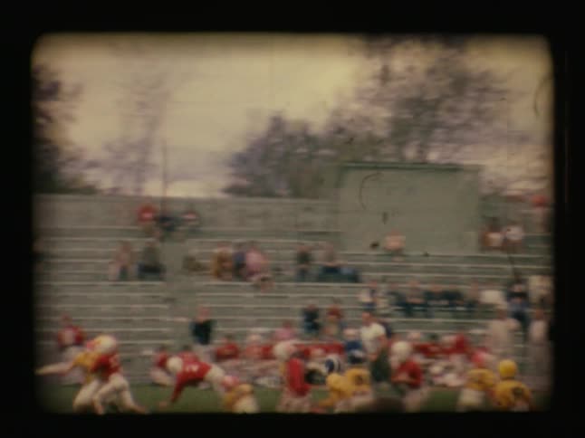 Boys compete on opposing football teams with spectators watching from bleachers