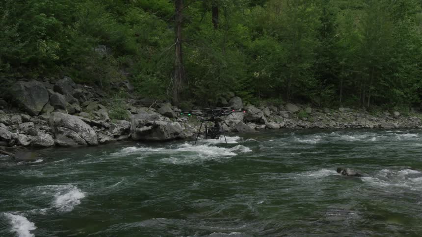 Drone flies over a flowing stream near the forest