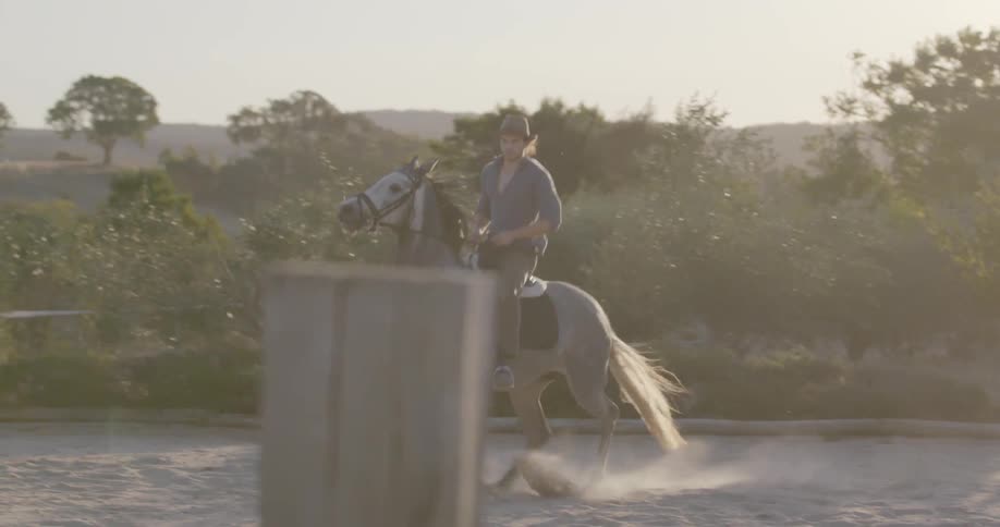 A man is riding his white horse in the sand