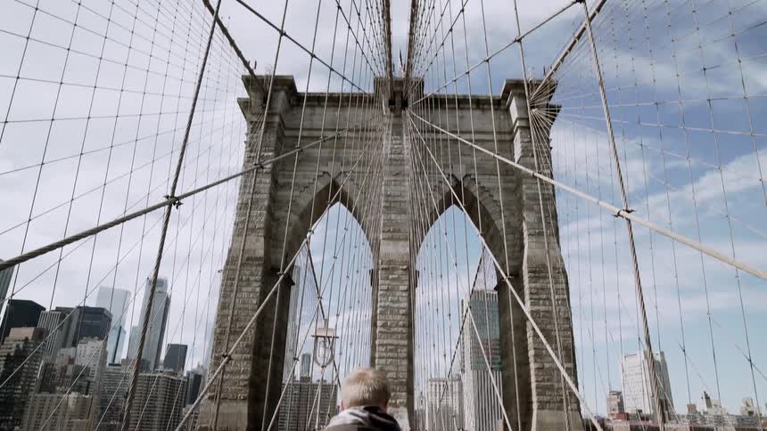 A man stands on a suspension bridge during a cloudy day