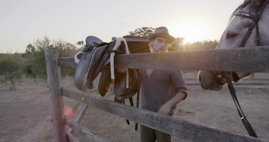 A man lifts a horse saddle onto a fence