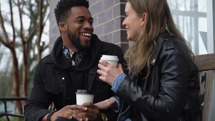 A man and woman sit close together as they talk outside a cafe