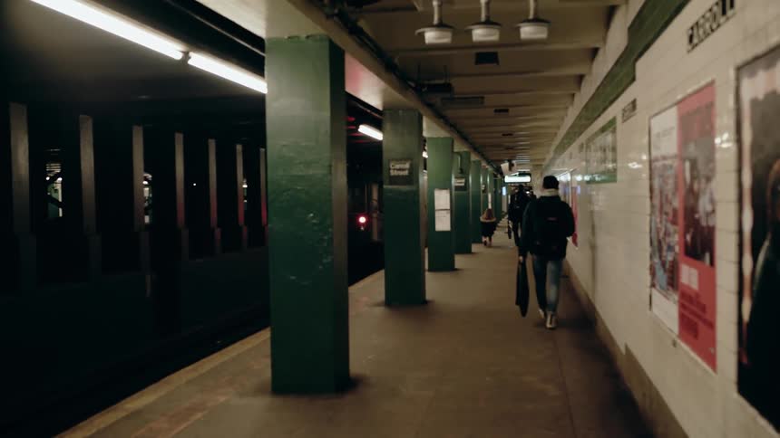 People walk through a subway station as a train passes