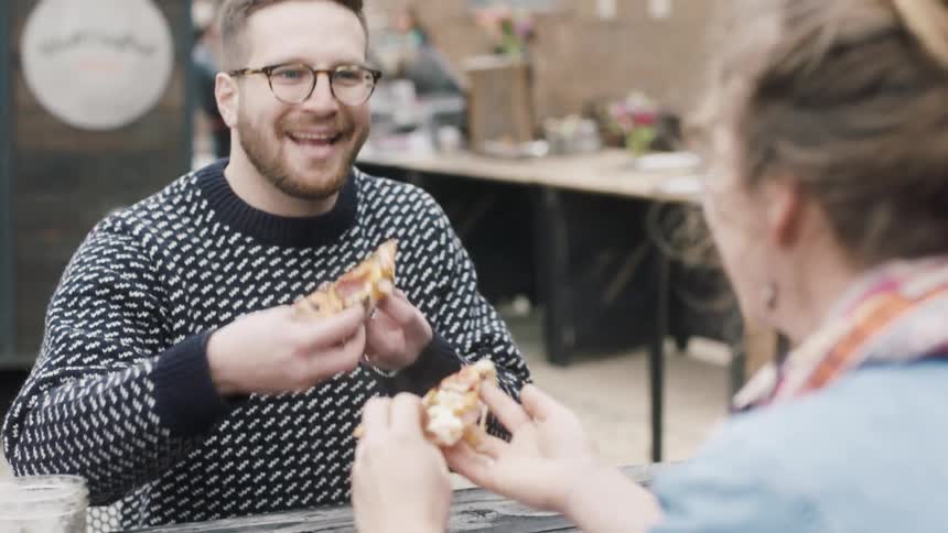 A man and woman pick up a slice of pizza and take a bite