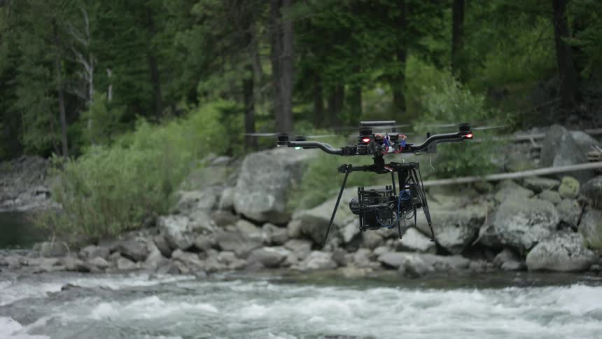 A drone flies over a rocky river in a forest during the day