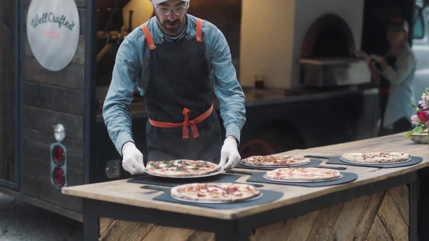 Workers prepare and serve pizza from a food truck during the day