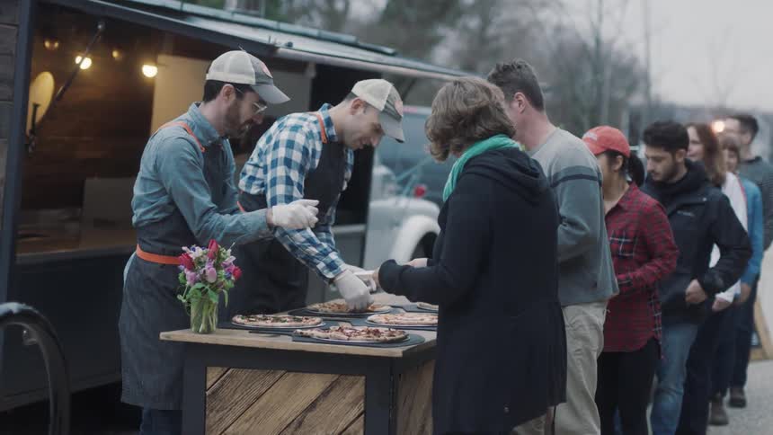 People line up to get pizza from a food truck