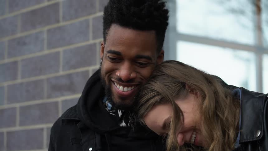A mixed race couple hug while sitting outside during the day
