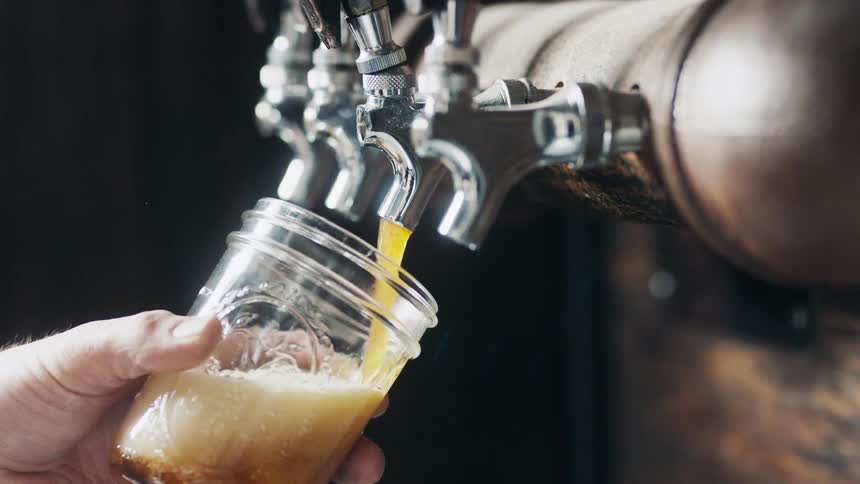 A drink is being poured into a glass from a spigot