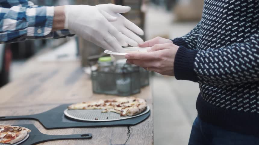 A man receives a slice of pizza from a vendor during the day