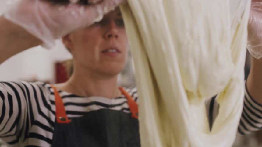 Woman wearing gloves lifts steaming dough with a utensil