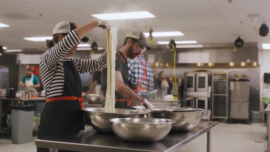 A group of people are making dough in a large kitchen