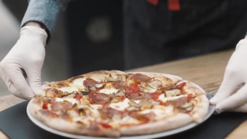A pizza chef places a baked pizza on a table