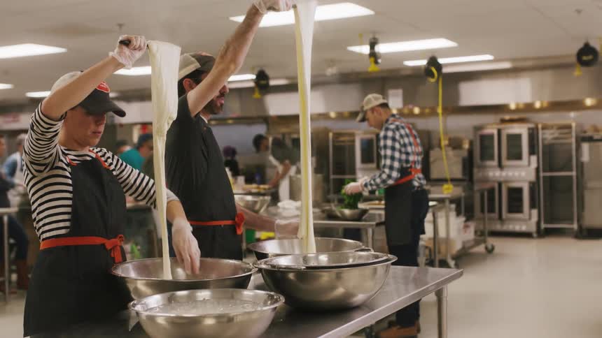 A group of chefs are instructed while making dough