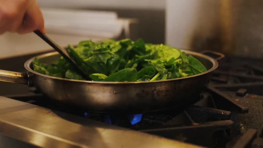 A chef stirs greens in a skillet