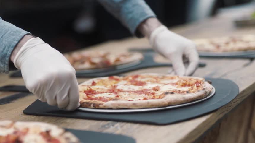 Man placing a pizza on a table next to others