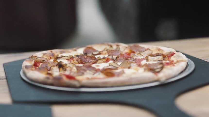 A man adjust the platter a cooked pizza is sitting on