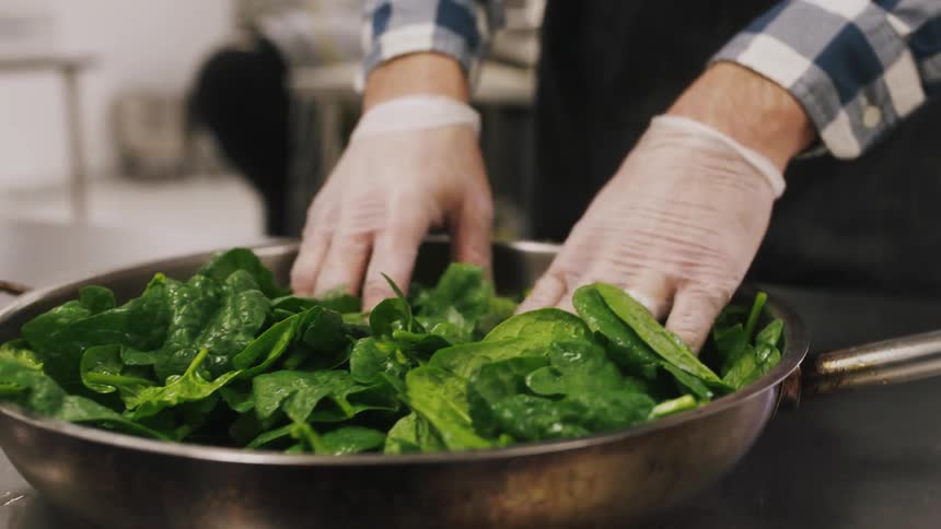 A chef is mixing fresh greens in a frying pan
