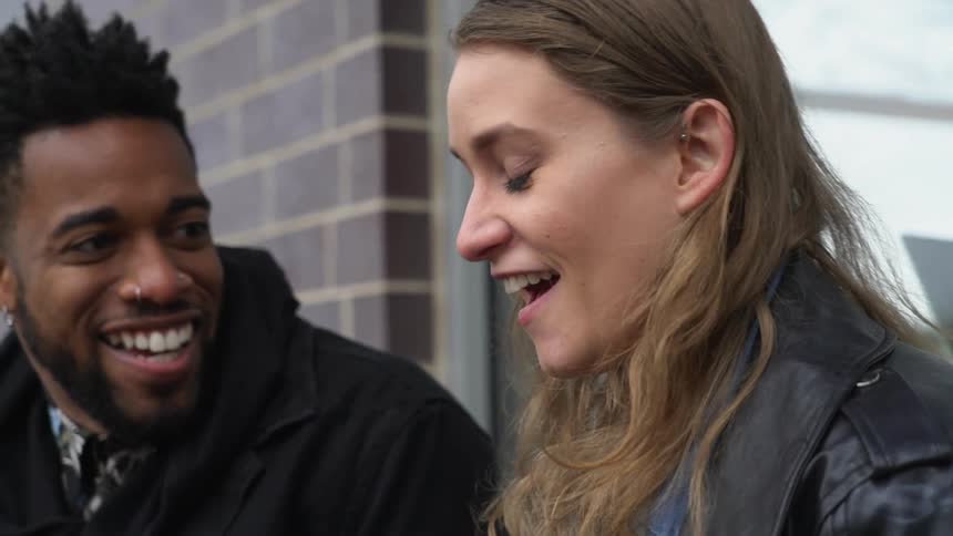 A man and woman laugh outside in front of a building