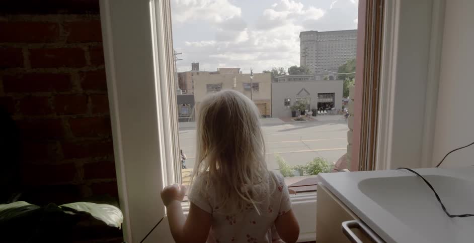 A young girl looks out the window at the street below