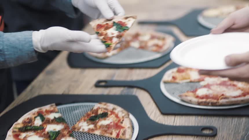 A worker hands a slice of pizza to a customer