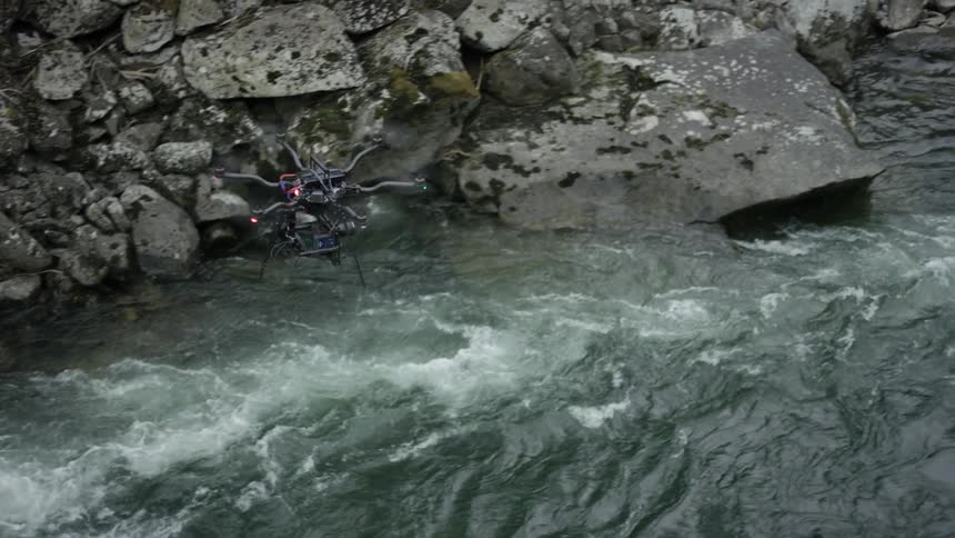 A drone flies over a flowing river with a rocky bank