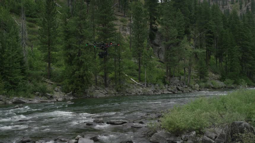 A drone flies over a river surrounded by trees