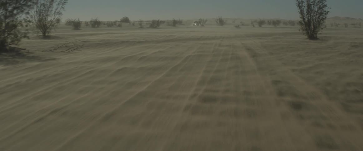 A vehicle with its headlights on travels over the sand