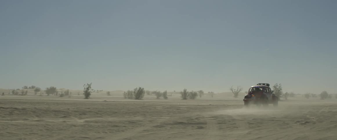 A vehicle races through the desert on a clear day