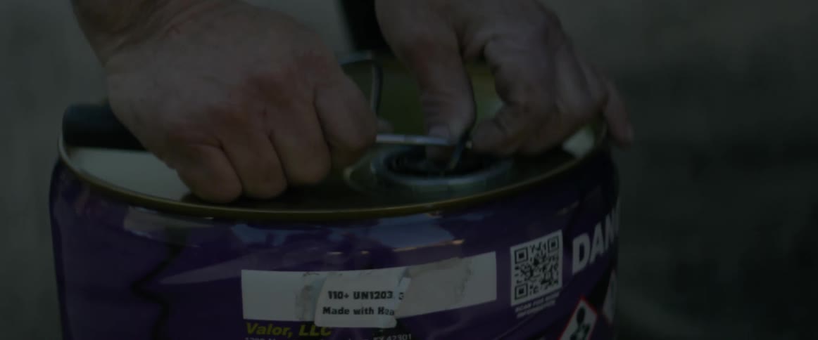 A man uses a flathead screwdriver to open a canister