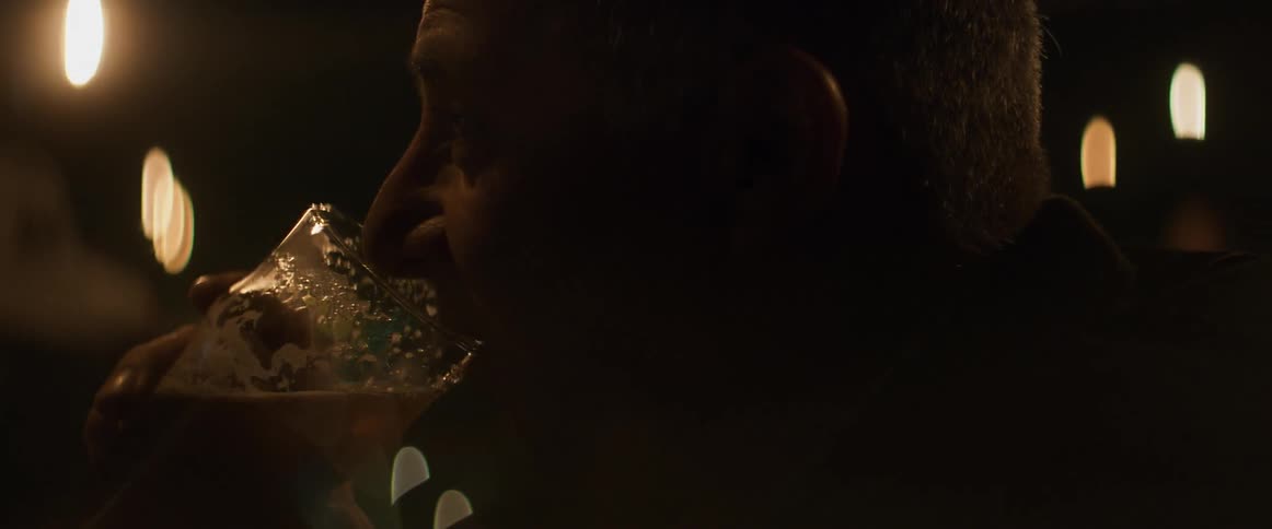 A man is drinking beer from a glass in a dimly lit room