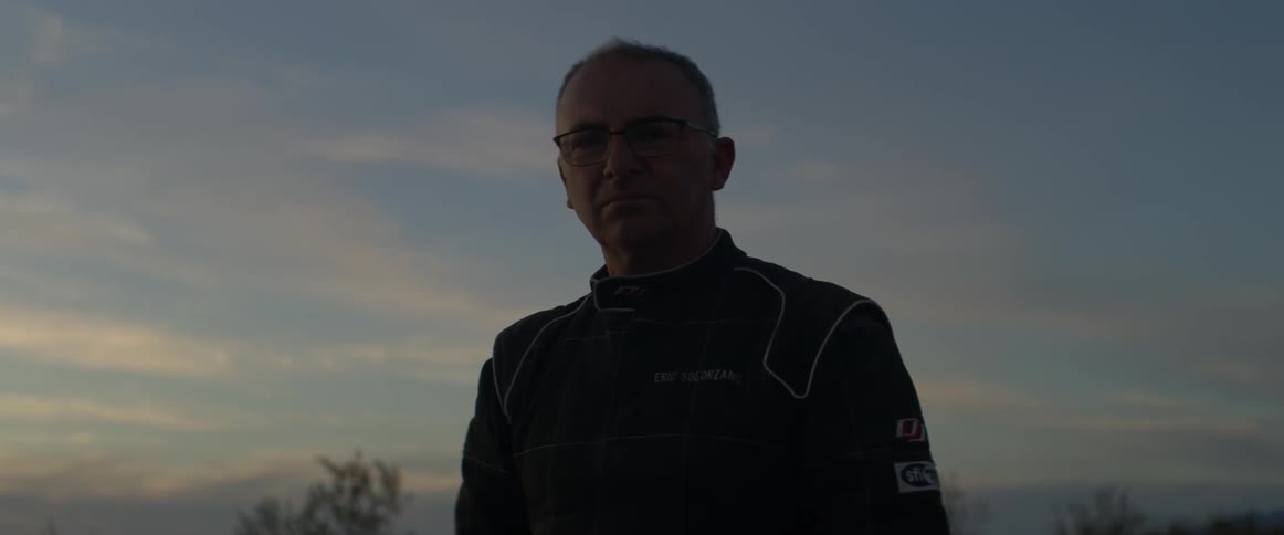 A man stares out at dusk wearing a racing suit